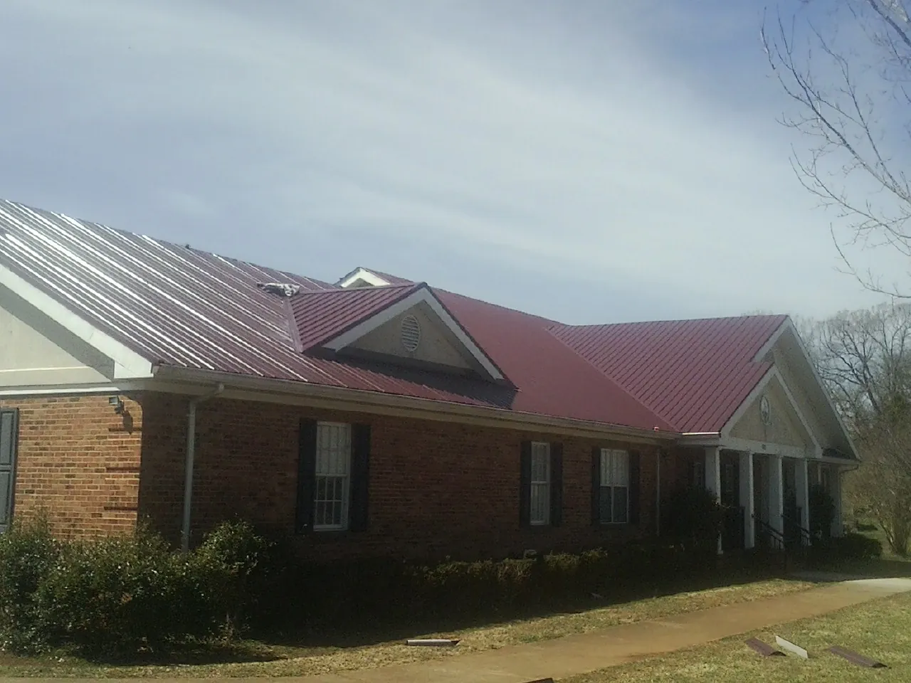 Red metal roof with gabled entries on a long brick building, from a Hail Damage Roof Repair job in Ramona
