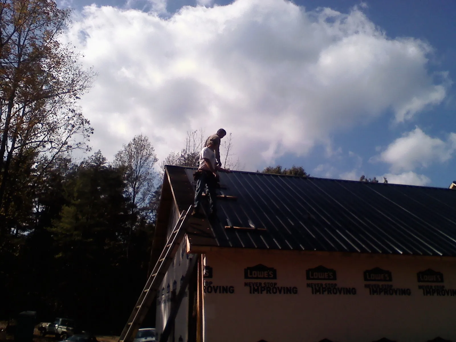 Roofer fastening dark metal panels high against a cloudy sky, from a Roof Inspection job in Ramona